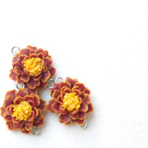 May include: Three polymer clay marigold flower charms in shades of red and yellow with silver jump rings.