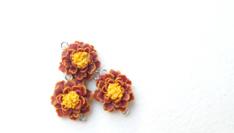 May include: Three polymer clay marigold flower charms in shades of red and yellow with silver jump rings.