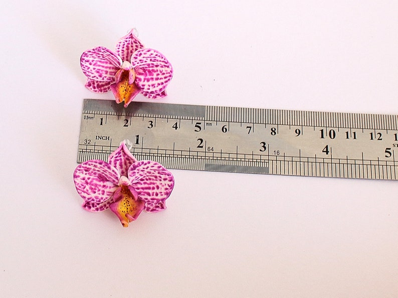 May include: Two pink and white orchid flower embellishments with yellow centres, measured against a ruler. The flowers are approximately 1 1/2 inches wide.