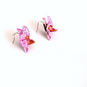 May include: A pair of pink and white orchid earrings with silver hooks. The orchids have a spotted pattern and a yellow centre.