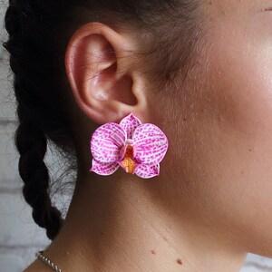 May include: A pair of pink and white orchid flower earrings. The earrings are made of polymer clay and have a realistic look.