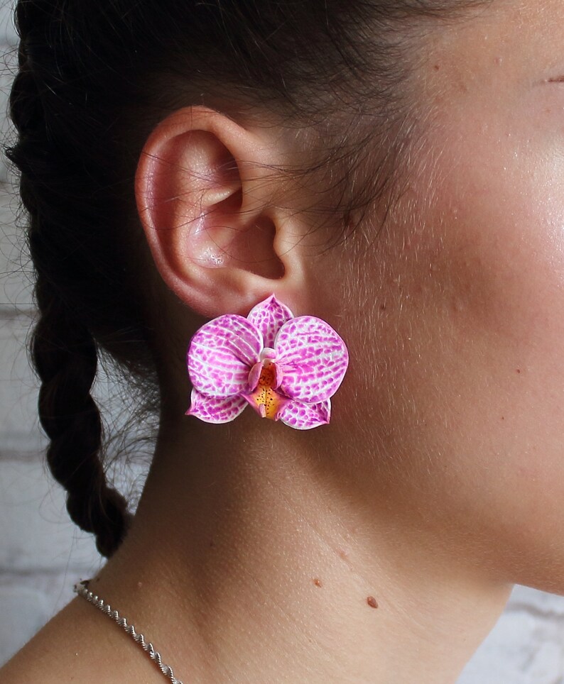 May include: A pair of pink and white orchid flower earrings. The earrings are made of polymer clay and have a realistic look.