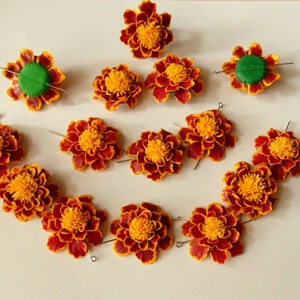 May include: A set of 12 orange and red marigold flower hair clips with green centers. The flowers are arranged in a semi-circle shape.
