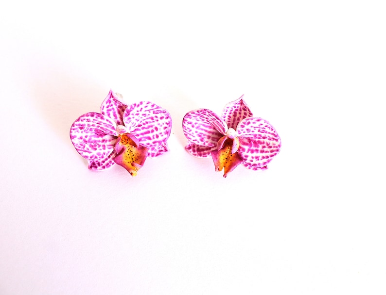 May include: A pair of pink and white orchid flower earrings. The flowers have a spotted pattern and a yellow centre.