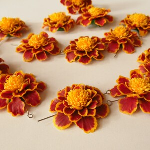 May include: A set of 12 orange and red marigold flower hair clips. The flowers are made of fabric and have a realistic appearance. The clips are attached to the back of the flowers.