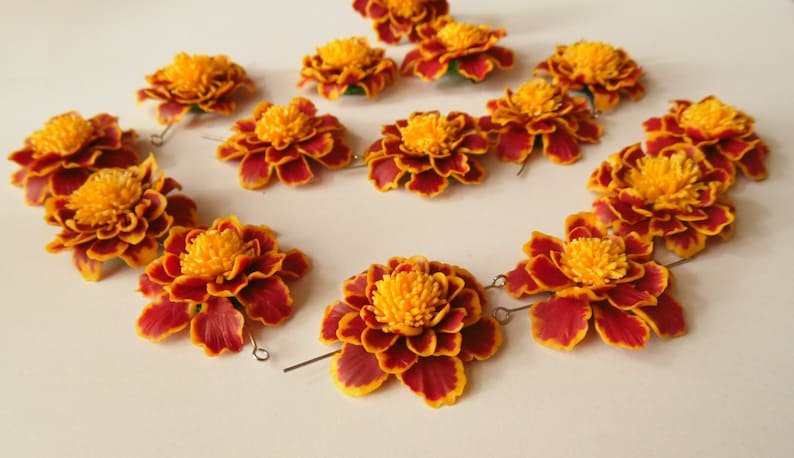 May include: A set of 12 orange and red marigold flower hair clips. The flowers are made of fabric and have a realistic appearance. The clips are attached to the back of the flowers.