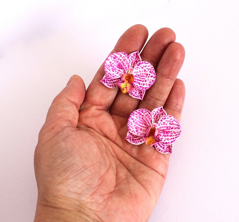 May include: Two pink and white orchid flowers with yellow centres, displayed on an open hand.