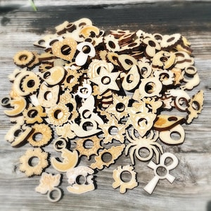 May include: A large pile of wooden charms with various designs, including a star, a spider, a crescent moon, a sunflower, and a heart. The charms are all made of light-colored wood and have a hole in the center.