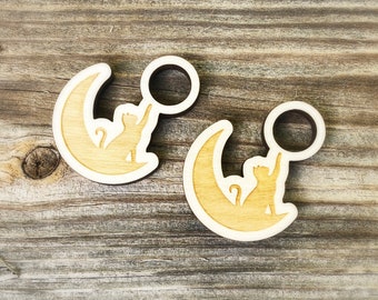 May include: Two wooden cat and moon ornaments. Each ornament features a cat reaching up to a crescent moon.