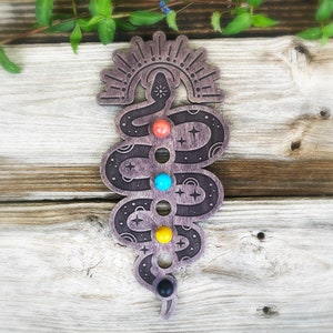 May include: Wooden snake with a sun and rainbow design, holding seven colorful stones in its coils. The snake is a chakra symbol and is a great addition to any home decor.
