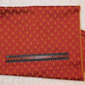 Könnte beinhalten: Roter Stoff mit einem goldenen Blatt-Muster. Der Stoff wird mit einem Lineal gemessen.