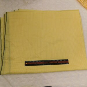 May include: A yellow gingham fabric with a white border. The fabric is folded and a ruler is placed on top of it.