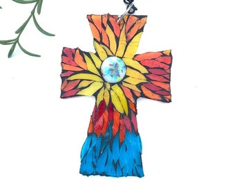 Peut inclure: Un pendentif en forme de croix fait à la main avec un motif de mosaïque. La croix présente un motif floral central en jaune et orange, passant au rouge et au bleu en bas. Il est suspendu à une chaîne noire.