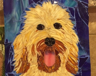 Könnte beinhalten: Mosaik-Kunstwerk, das das Gesicht eines Hundes darstellt. Der Hund hat ein hellbraunes, zotteliges Fell, schwarze Augen und eine rosa Zunge. Der Hintergrund ist ein Mosaik aus blauen und türkisfarbenen Glasstücken.