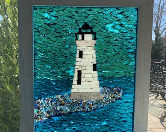 Könnte beinhalten: Gerahmtes Mosaikkunstwerk eines Leuchtturms. Der weiße Leuchtturm mit schwarzem Dach steht vor einem türkisblauen Hintergrund. Der graue Rahmen umgibt das Kunstwerk, das an einer Kette aufgehängt ist.