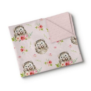 Könnte beinhalten: Eine rosa Babydecke mit einem sich wiederholenden Muster aus Aquarell-Igeln und Blumenarrangements. Die Igel sind braun und grau, umgeben von rosa und pfirsichfarbenen Rosen und grünen Blättern. Die Rückseite ist einfarbiger, strukturierter rosa Stoff.