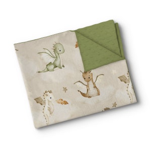 Puede incluir: Una manta para bebé plegada con un diseño de dragones en verde, marrón y blanco sobre un fondo beige. El reverso es verde oliva liso con un patrón texturizado. El diseño incluye ilustraciones de dragones y estrellas.