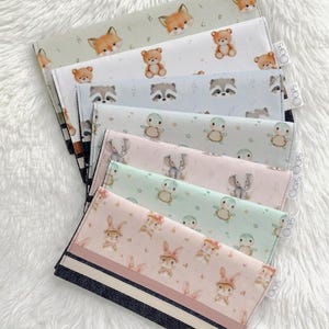 May include: A collection of rectangular fabric pouches featuring various animal prints including foxes, bears, raccoons, penguins, elephants, and rabbits. Each pouch has a small white tag labelled OOPS on the side and a solid coloured fabric base.