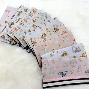 May include: An assortment of folded fabric pieces featuring diverse patterns, such as tractors, animals, and floral motifs. The fabrics are fanned out on a white, fluffy surface. The colour scheme incorporates gentle pastels and earthy tones.