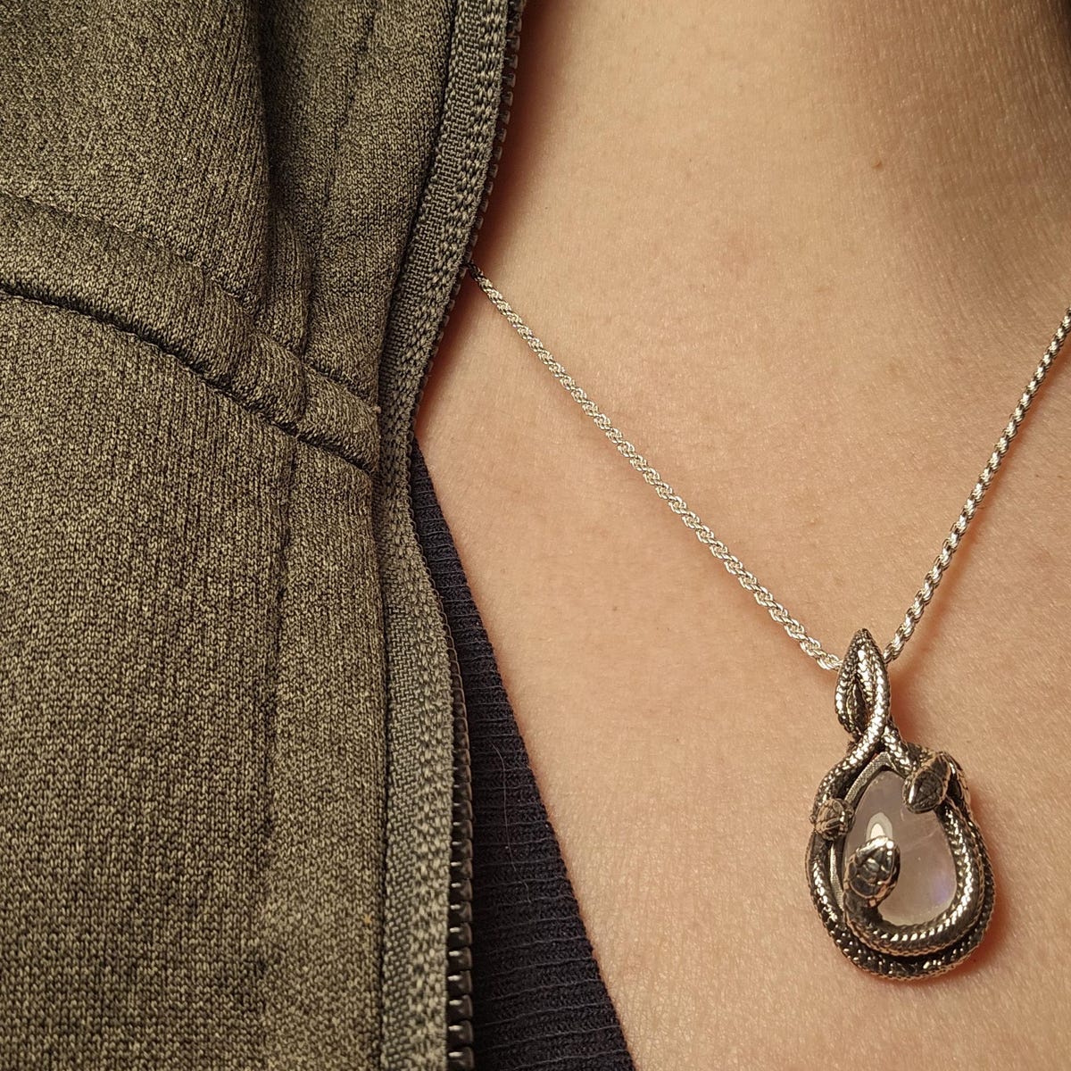 Snake-wrapped moonstone pendant necklace in sterling silver, worn on a person wearing open green hoodie.