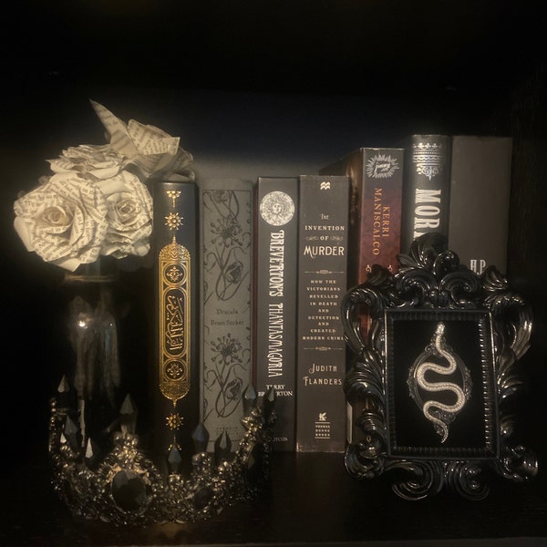 Gothic bookshelf with black rose bouquet, ornate crown, and framed silver snake wall art displayed among Victorian-themed books