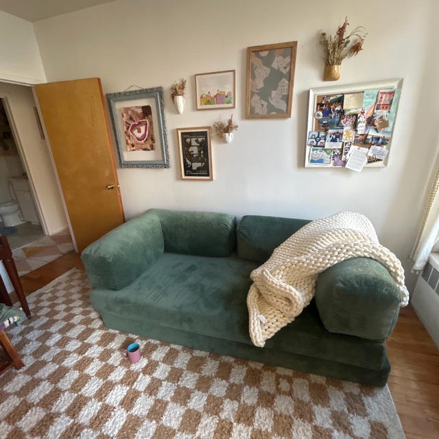 Sage green corduroy sofa with a knitted throw on a chequerboard floor below a gallery wall, photographed by the buyer