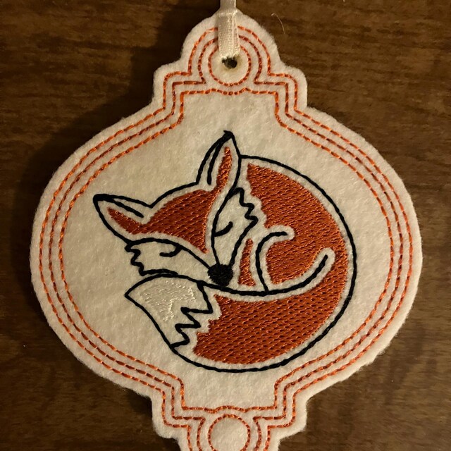 刺繍された眠そうなキツネのクリスマスオーナメントのデザイン