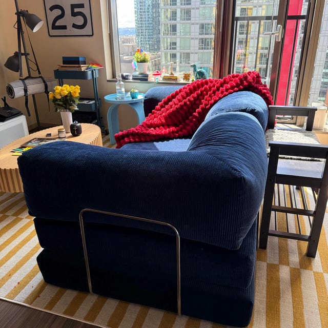 Navy blue corduroy sofa in a bright city apartment with a red throw, photographed by the buyer