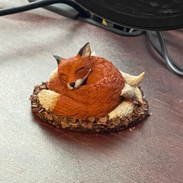 Figurine miniature de renard roux dormant dans une tasse de thé