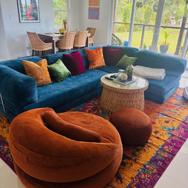 Teal blue corduroy sofa with rust poufs on a bright patterned rug in a sunroom, photographed by the buyer