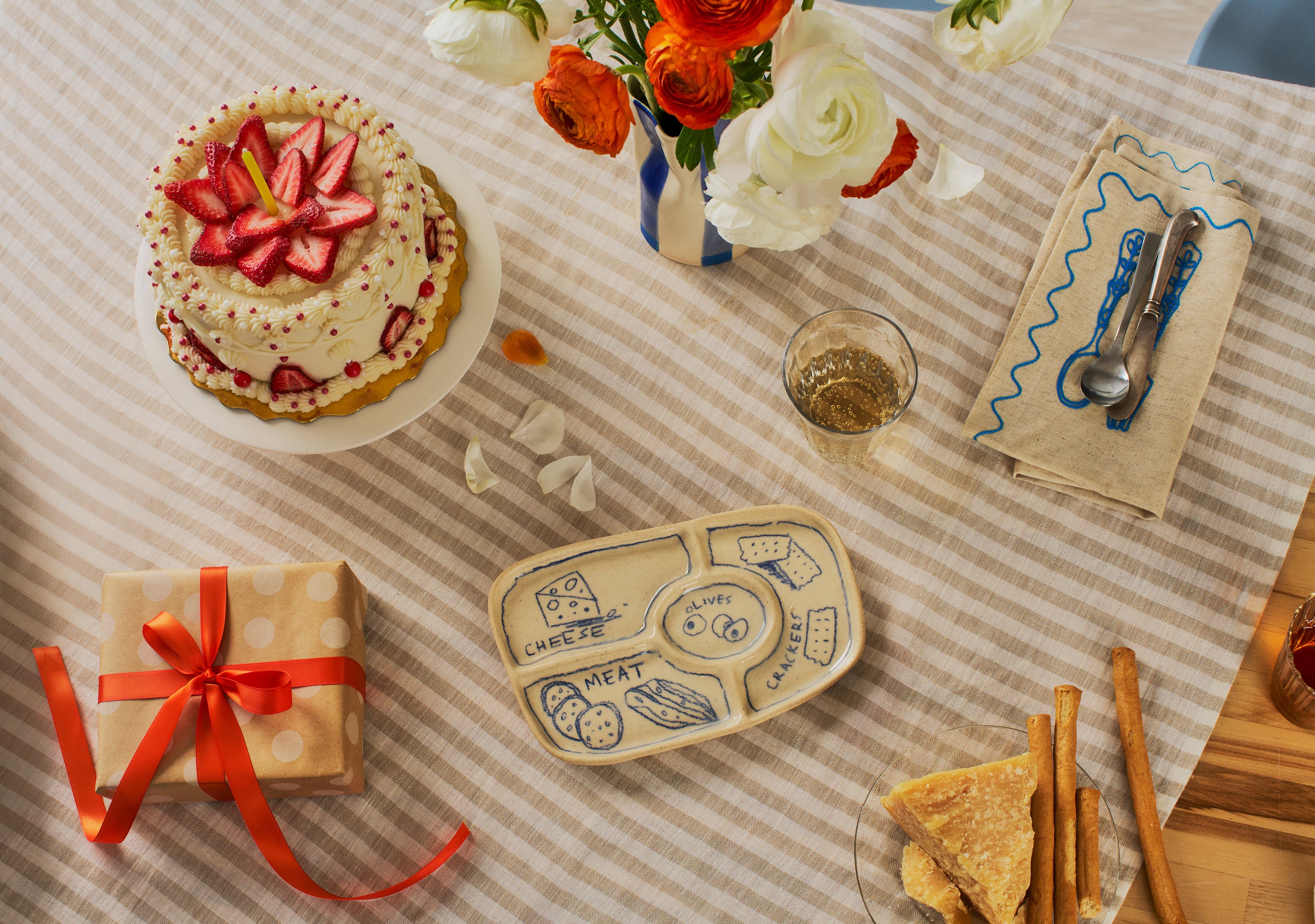A table setting with a strawberry cake, blue and white vase, a gift and other dinnerware.
