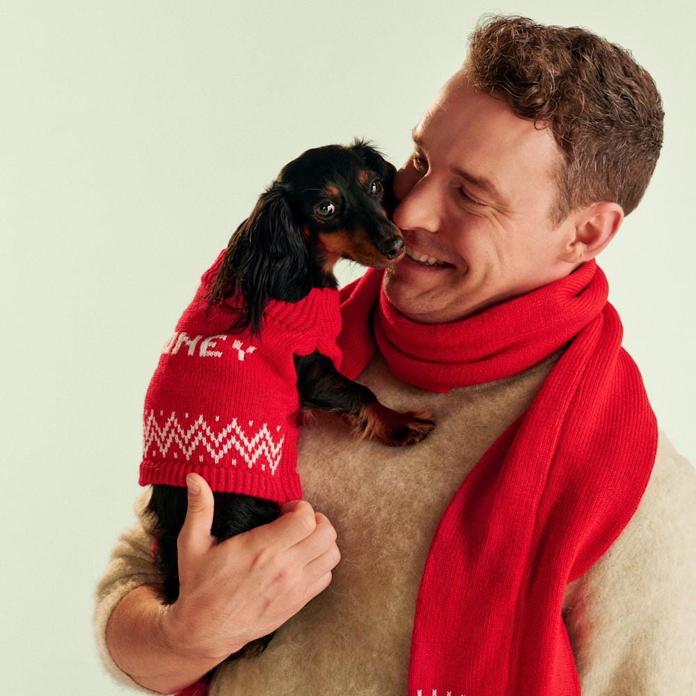 Mann mit rotem Schal hält einen kleinen schwarzen Hund im Arm, der einen personalisierten Pulli trägt