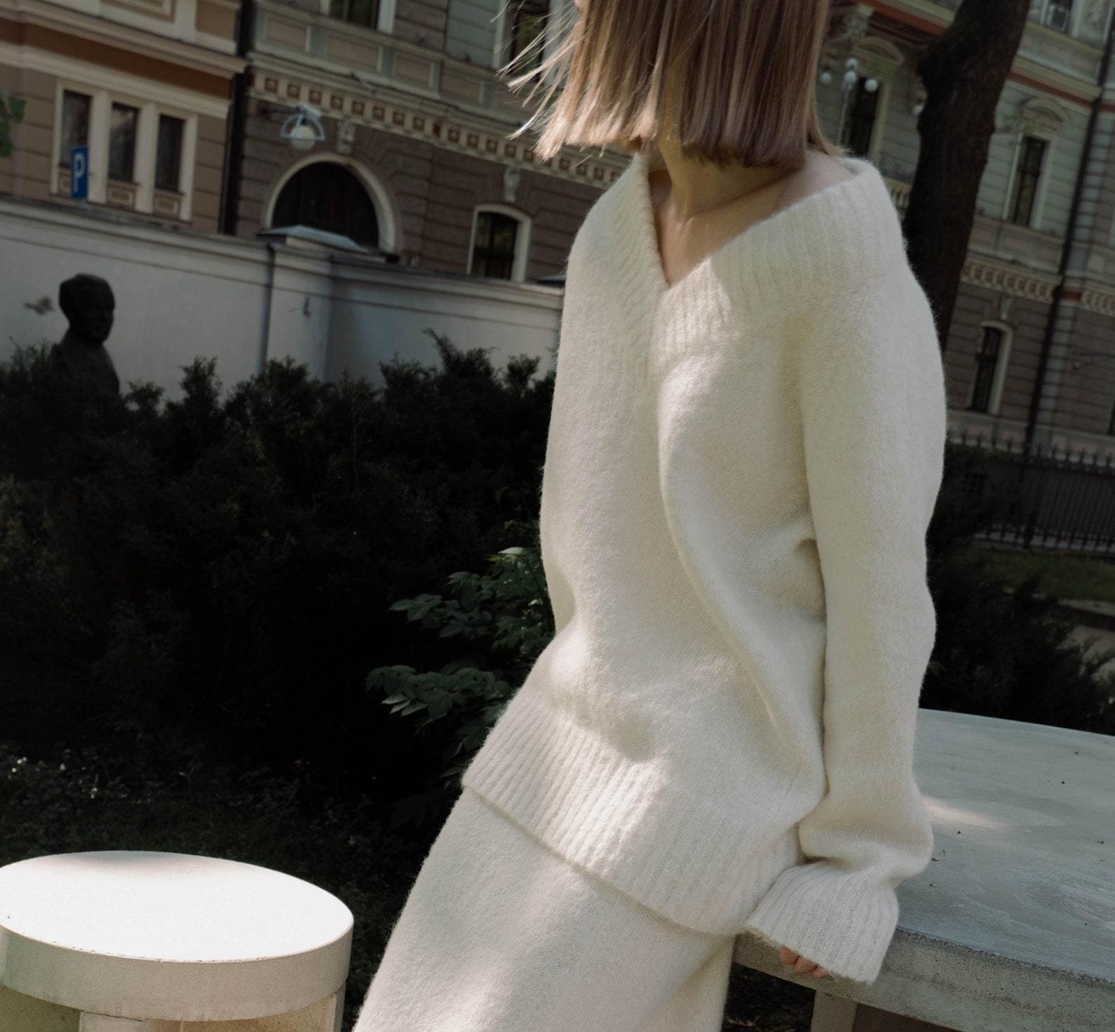 A woman wears a white, v-neck sweater.