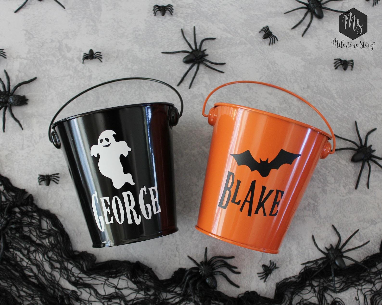A pair of orange and black personalized trick or treat tin buckets.