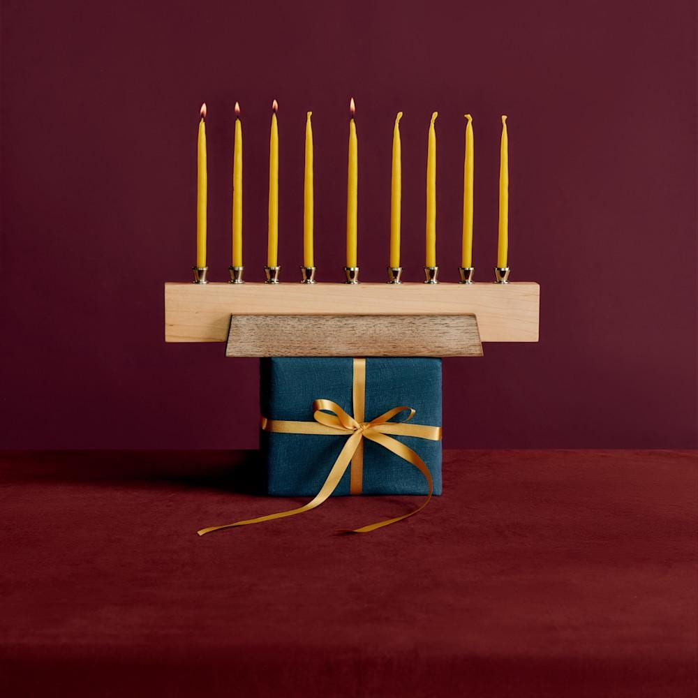 Menora aus Holz auf einem Geschenk in blauem Einwickelpapier und goldgelbem Band