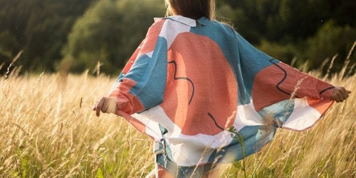 A joyful person running through a field wearing a linen shirt that has a multi color white, peach, and teal print.