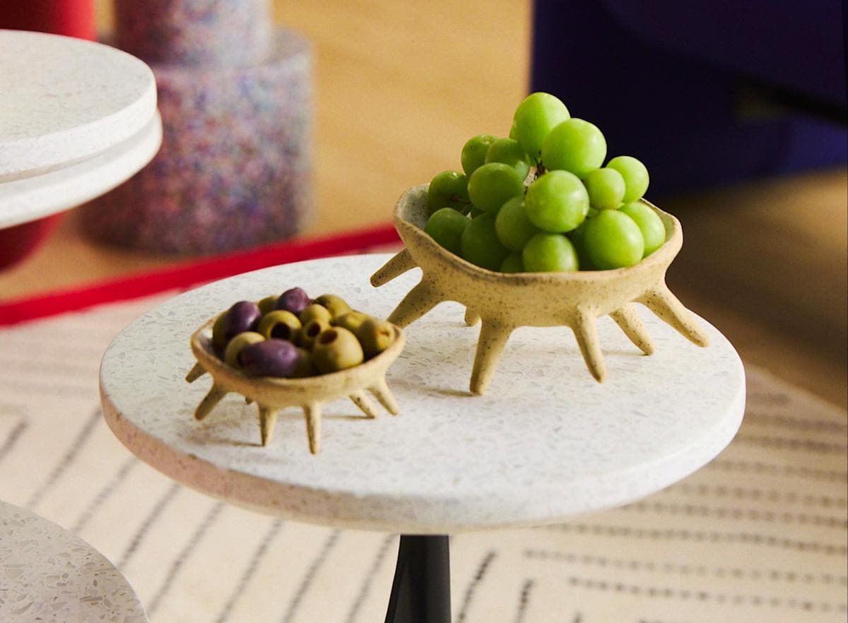 two small ceramic trays sit atop a bistro table, holding grapes and olives.