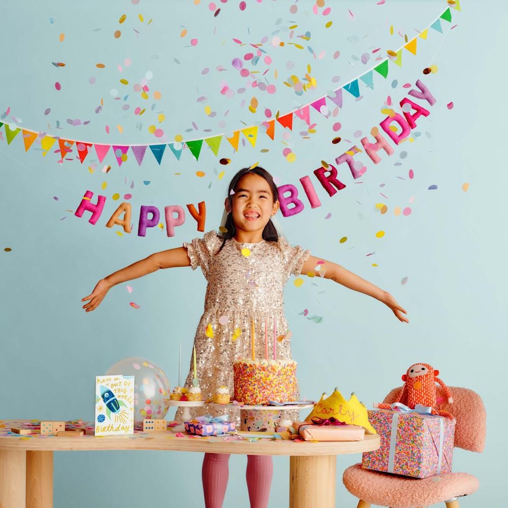 Una niña pequeña debajo de un cartel en el que se lee Happy Birthday, con confeti cayendo