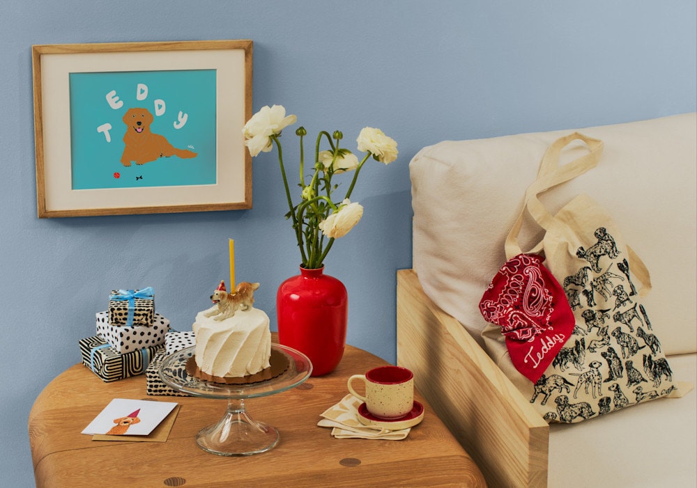 A dog birthday celebration with a cake, personalized portrait and red bandana and dog tote.