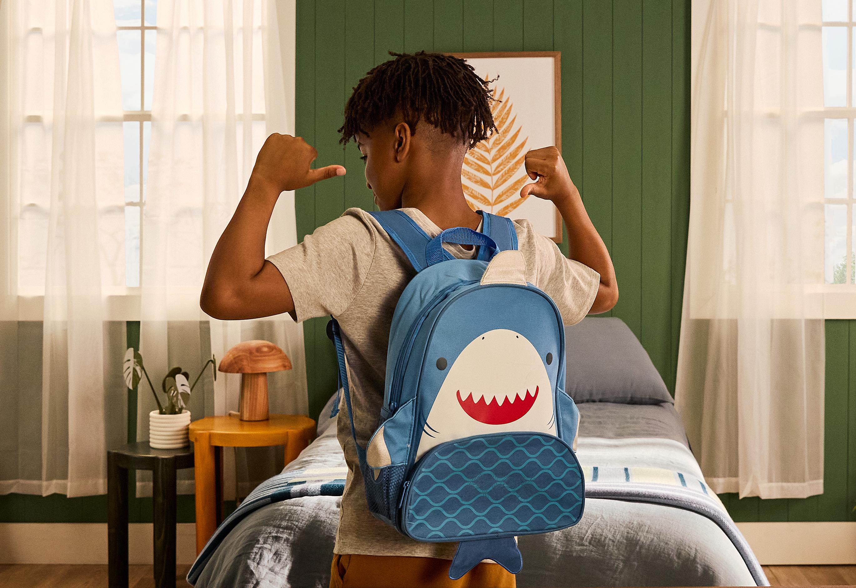 A young boy is wearing a shark themed backpack.