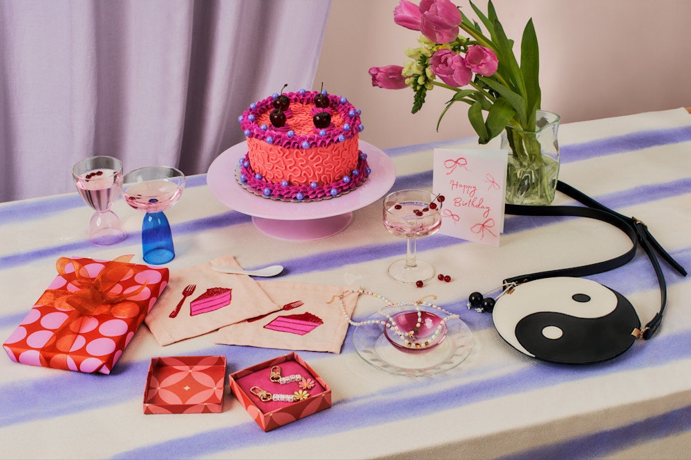 A table set with pink, purple and birthday decorations and gifts.
