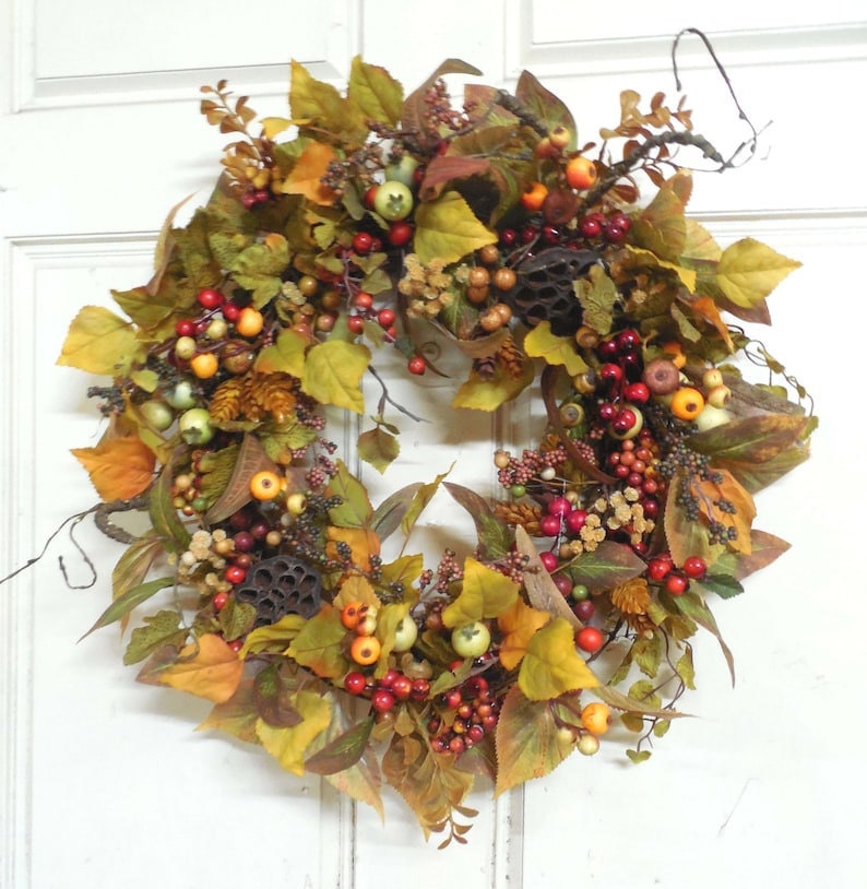 A welcome fall wreath with berries and fall foliage and greenery hanging on a white door.