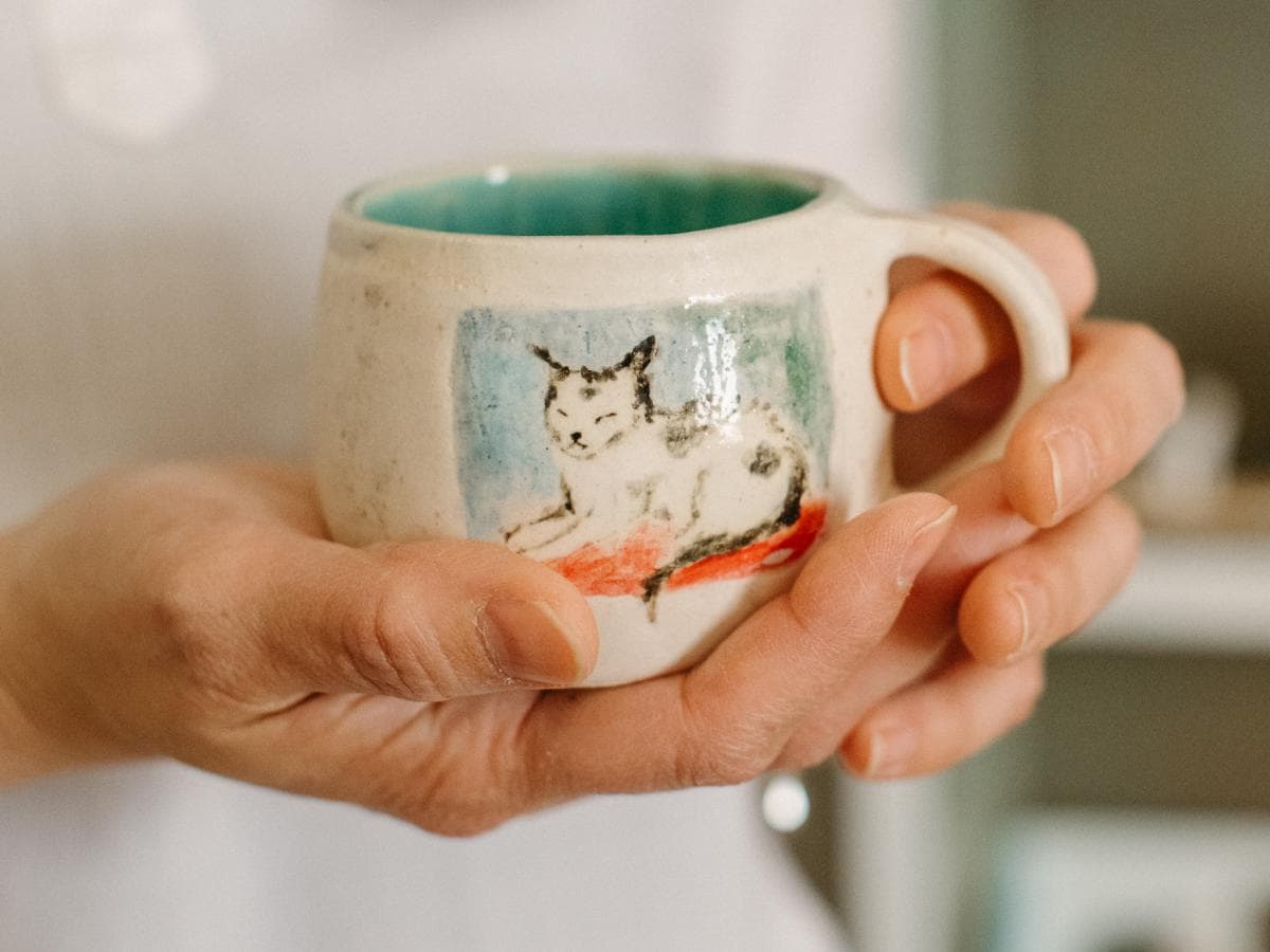 Porcelain mug painted with a sleepy cat illustration by Winking Cat Clay.