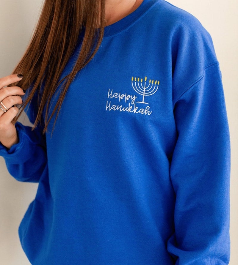 A woman wearing a blue crewneck sweatshirt embroidered with