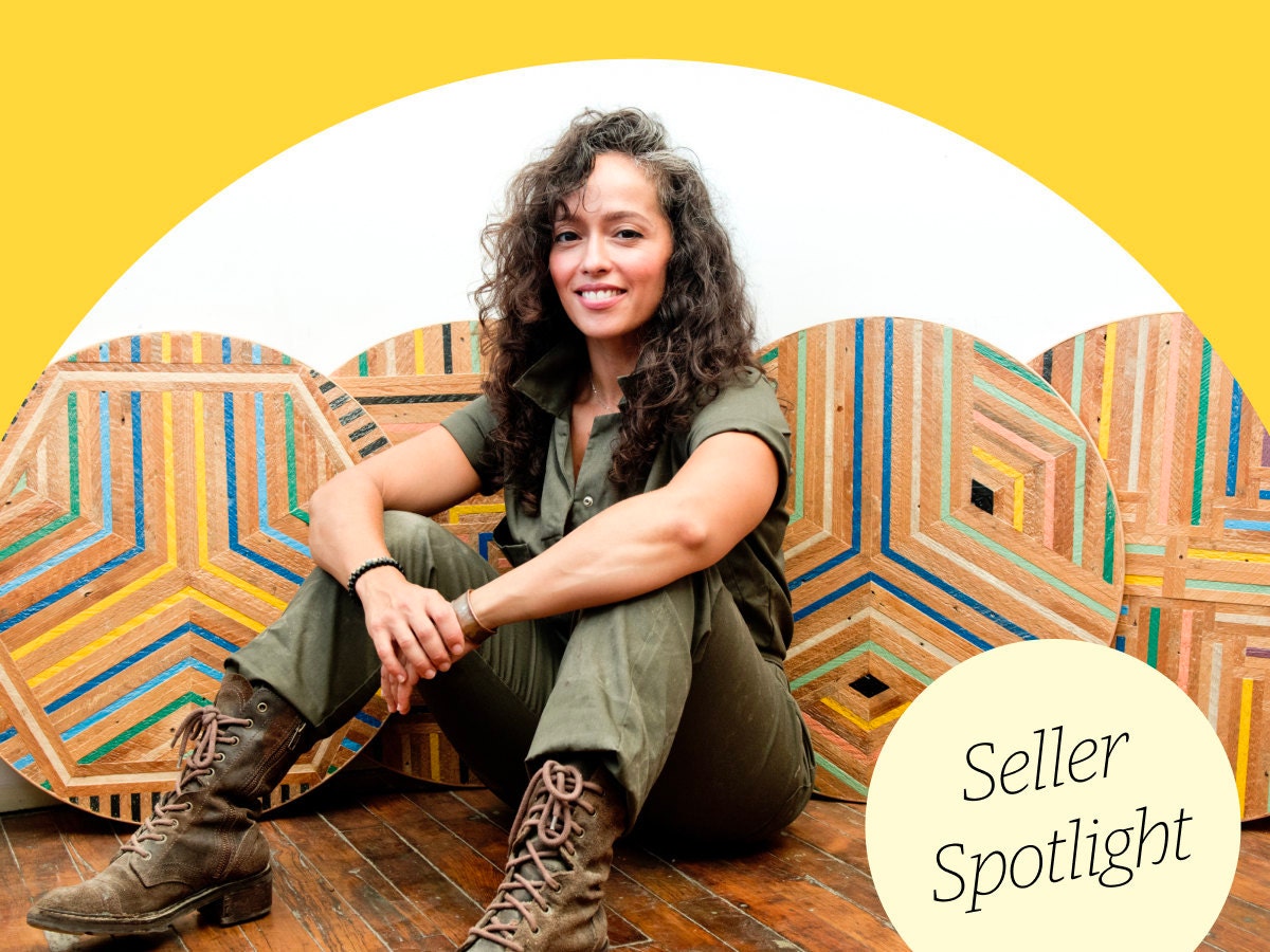 Tiffany Gomez sits facing the camera in front of four colorful tabletops propped against a white wall Tiffany Gomez sits facing the camera in front of four colorful tabletops propped against a white wall