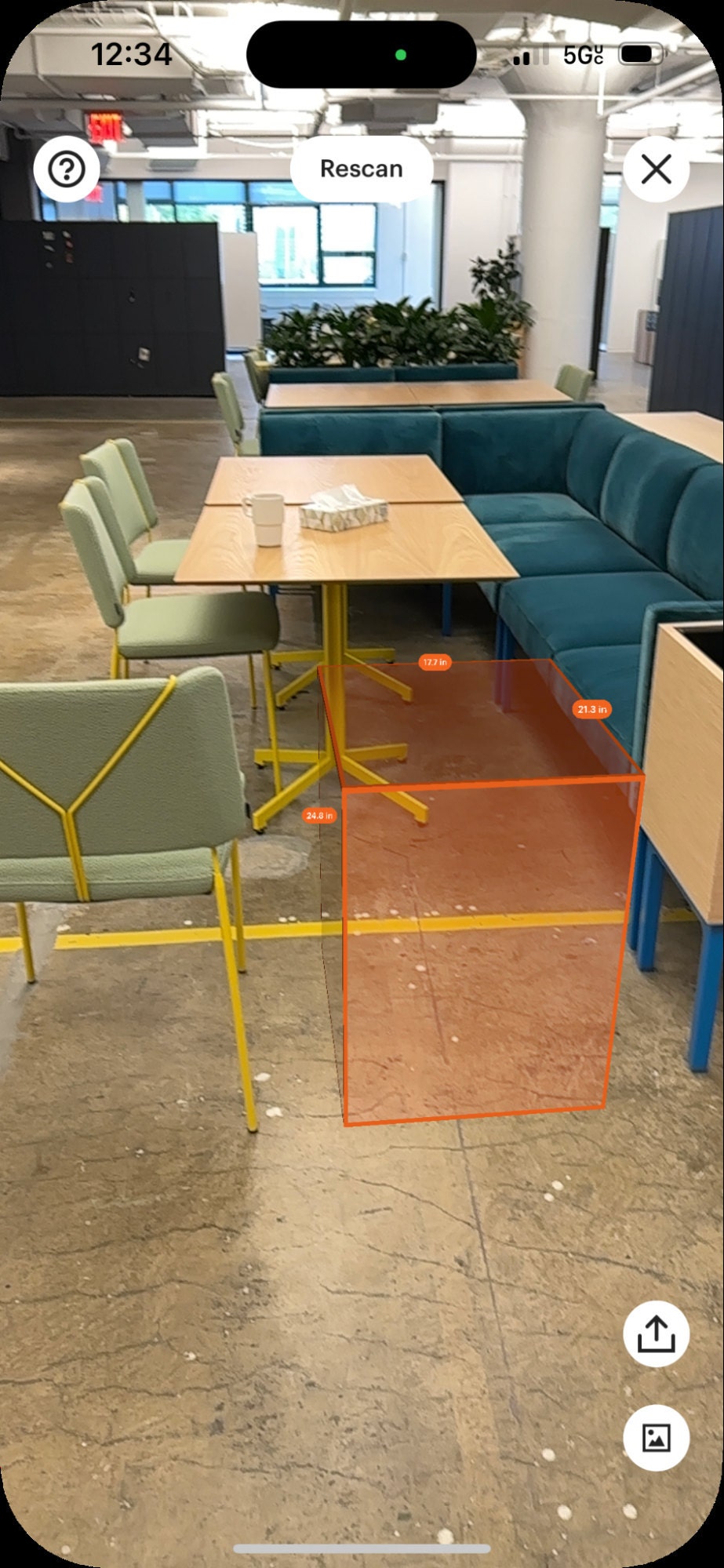 An orange rectangular prism placed in between furniture with measurements shown on each edge of the prism