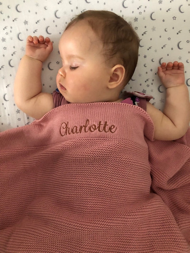 A baby sleeps under a pink personalized baby blanket embroidered with the name Charlotte