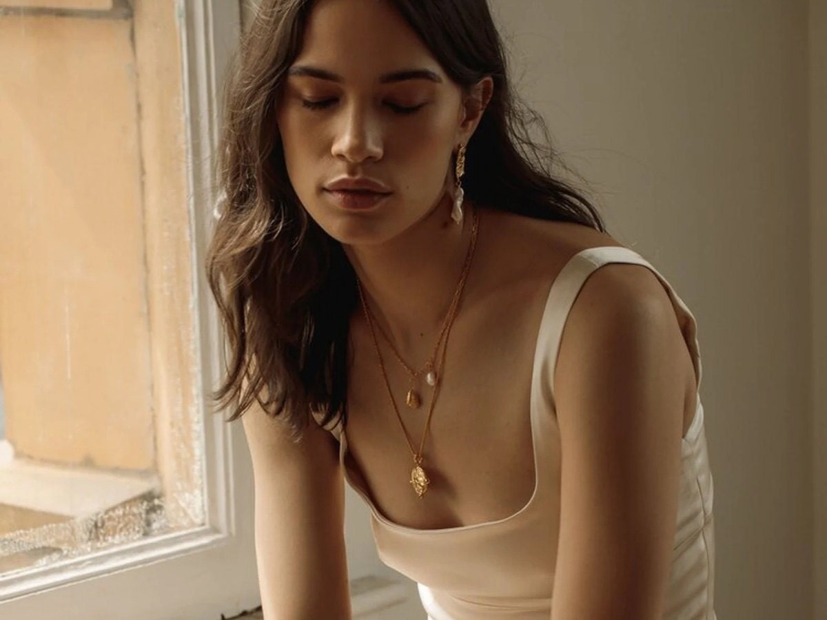 How to layer necklaces: A model wearing a three-necklace stack featuring gold necklaces with charms How to layer necklaces: A model wearing a three-necklace stack featuring gold necklaces with charms
