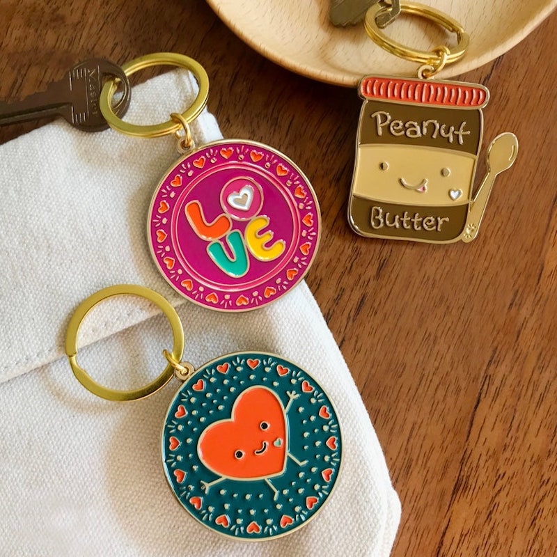 Three enamel keychains from Etsy on a wood surface