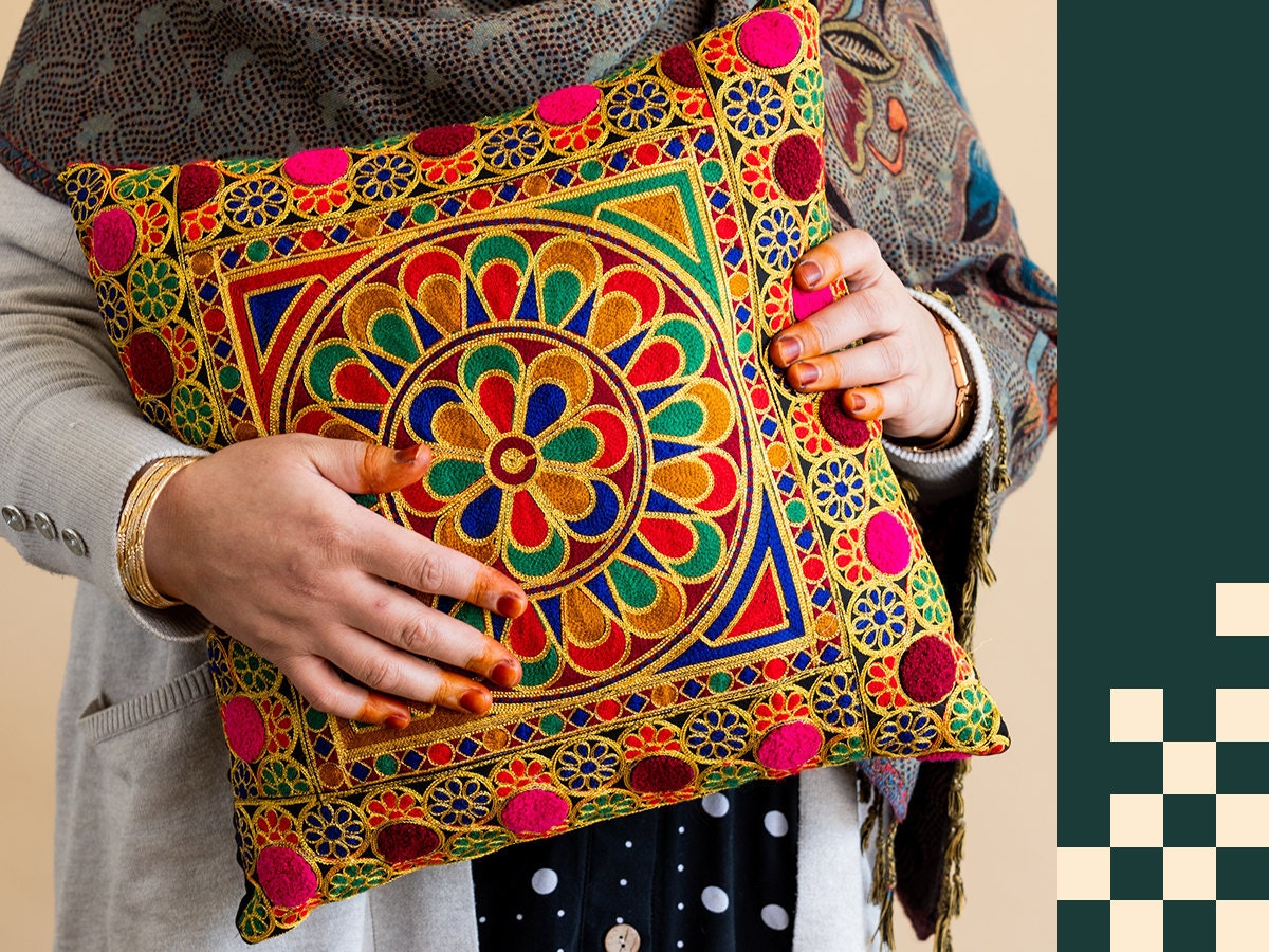 A member of the Afghan Refugee Collective holds a hand-embroidered pillow of her own making. A member of the Afghan Refugee Collective holds a hand-embroidered pillow of her own making.